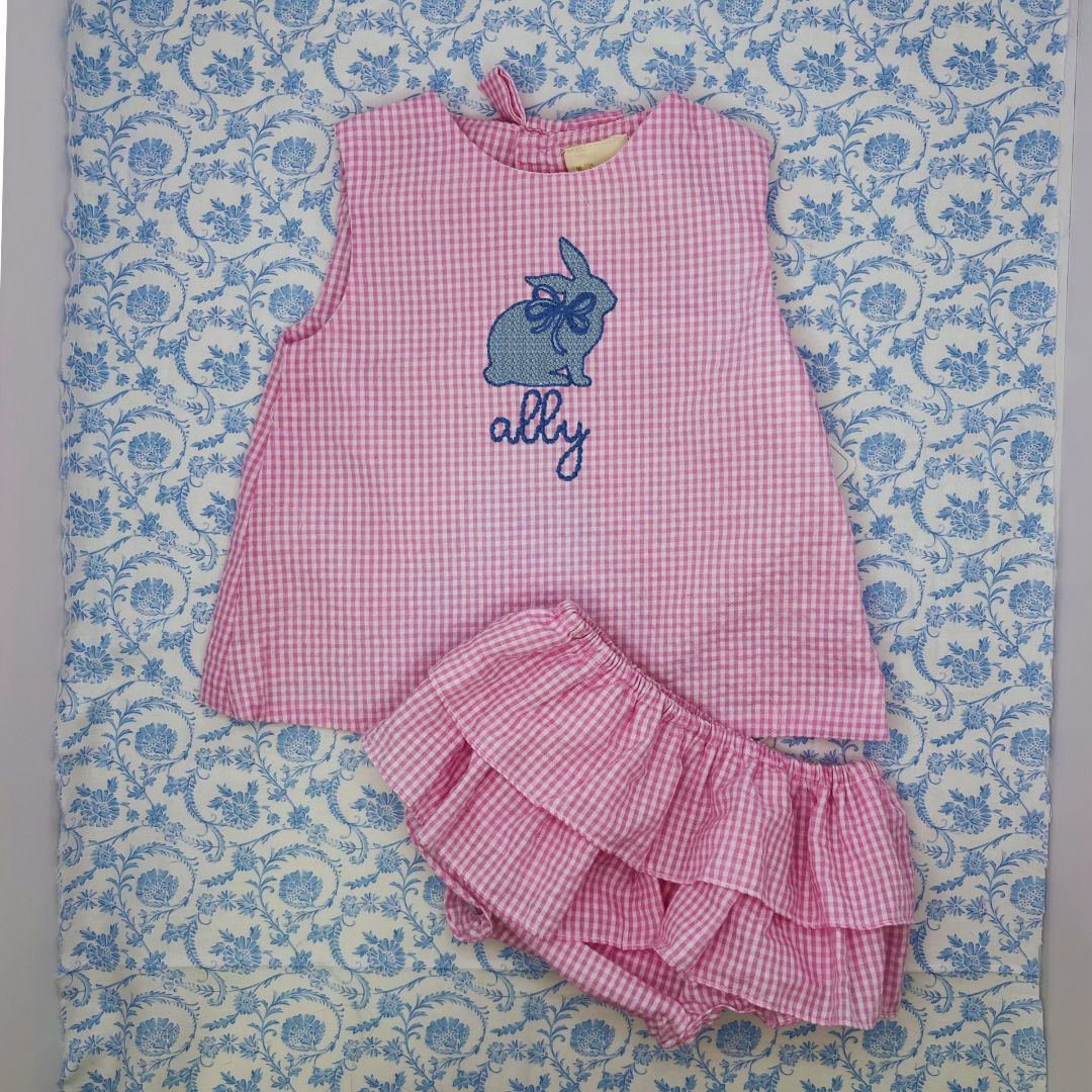 The Petit Ami Pink Check Seersucker Pop Over is a unique and stylish choice for your little one. This popover features a ruffle diaper cover and is made of high-quality seersucker material. Add a personalized touch with custom embroidery. Elevate your child's wardrobe with this charming addition.